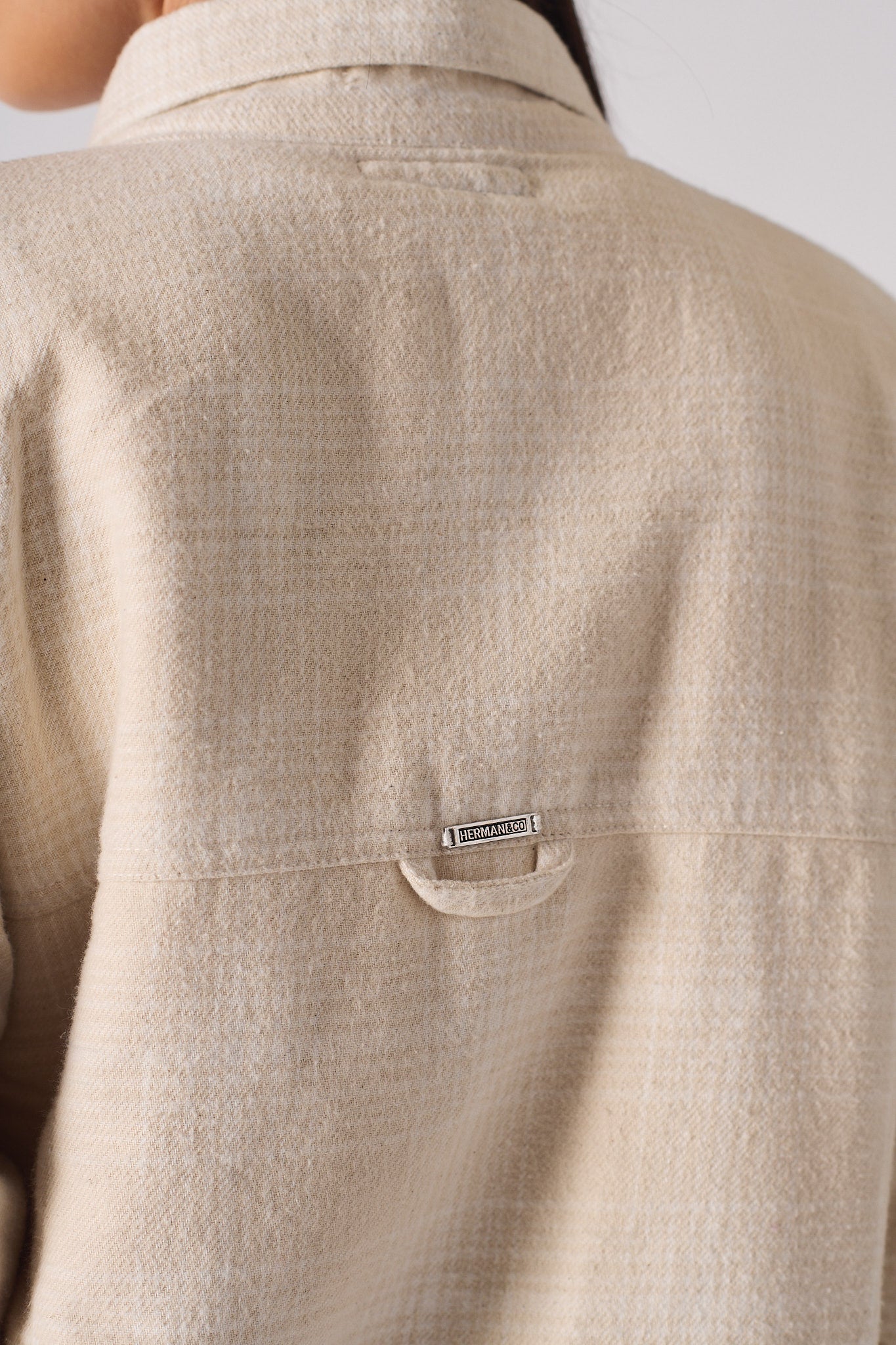 Close-up of the metal logo detail on the back of the beige check shirt.