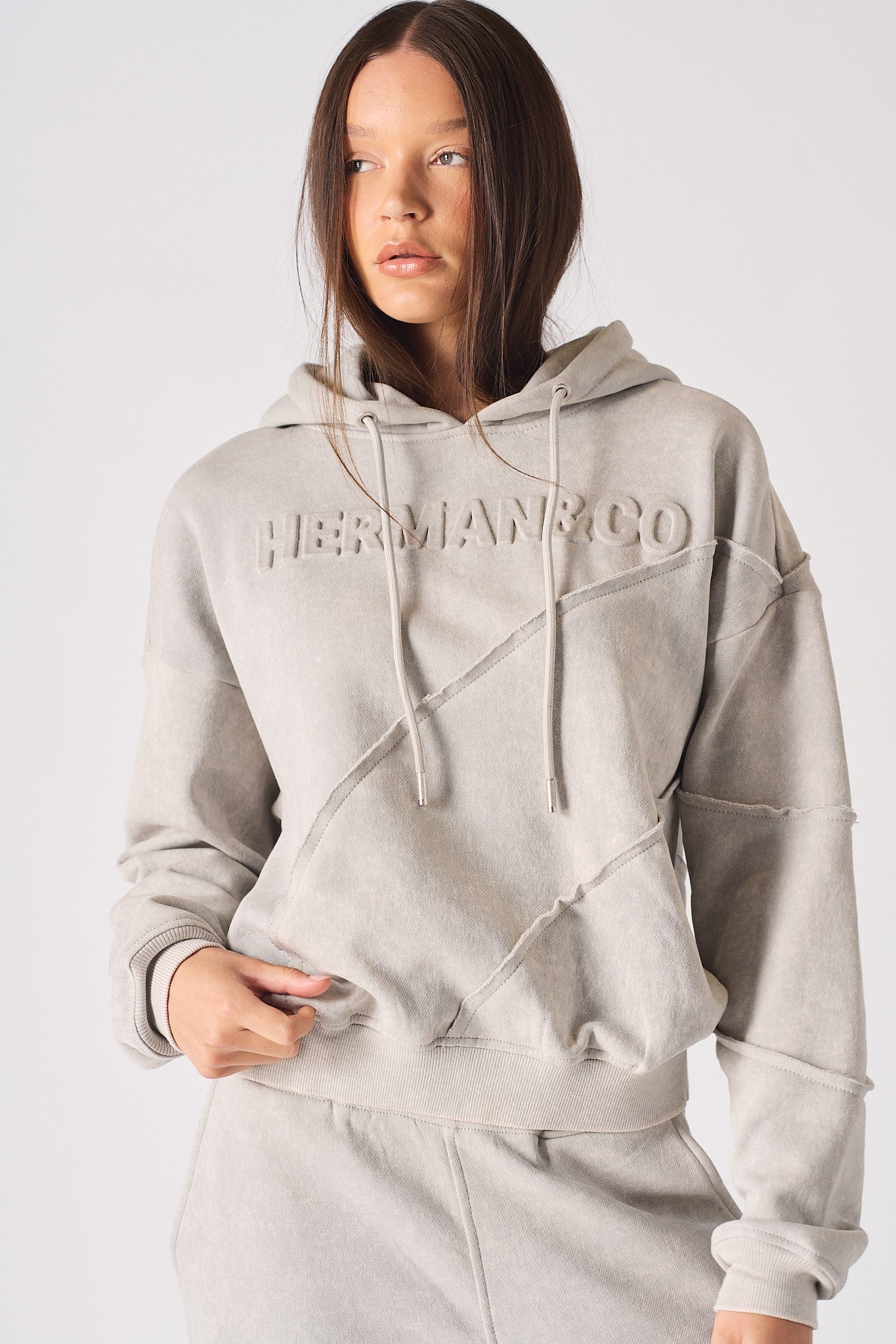 Close up detail of the embossed HERMAN logo on the chest of womens grey hoodie