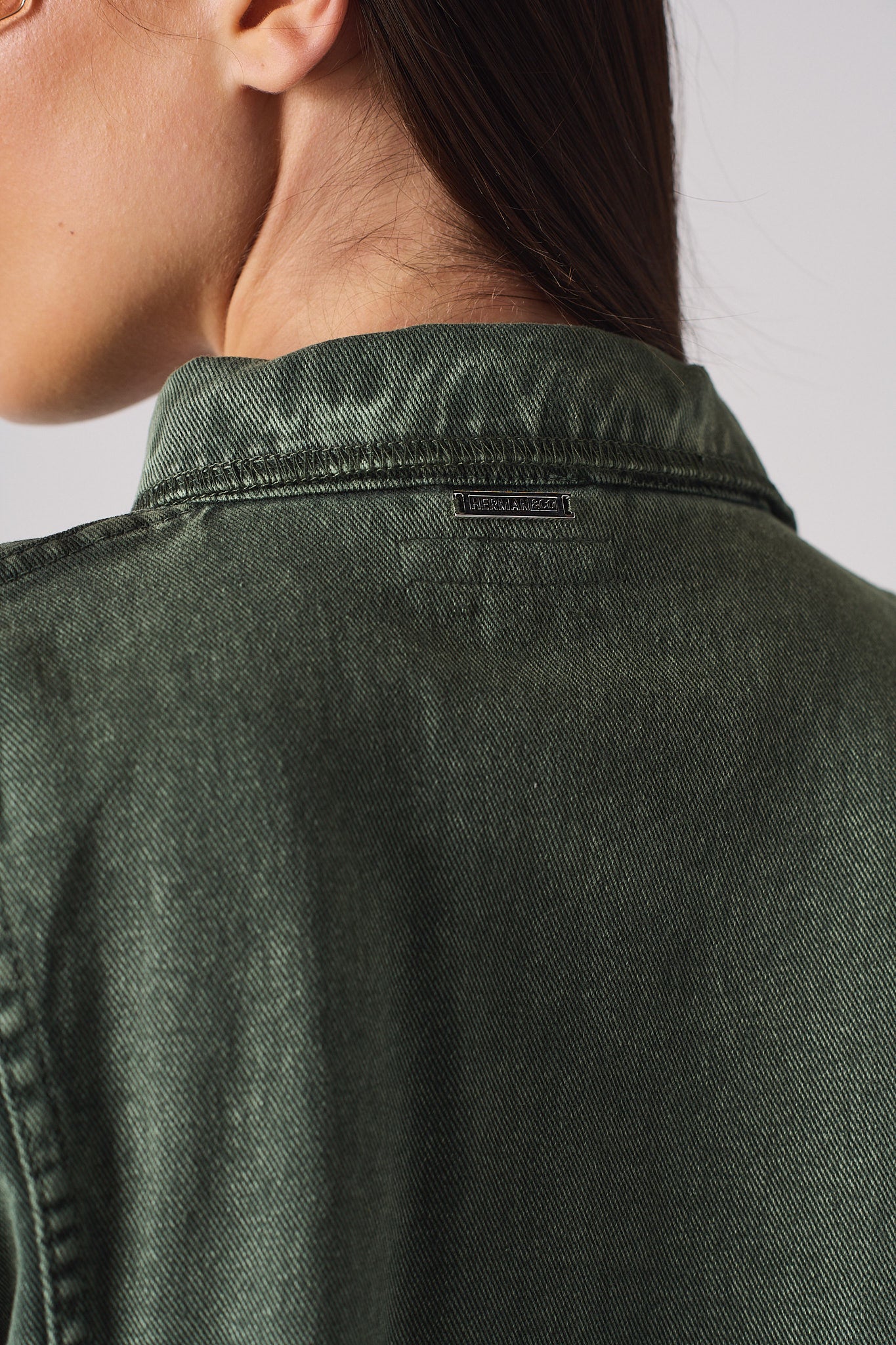 Close-up of the branded metal tag on the collar of the green denim shirt.