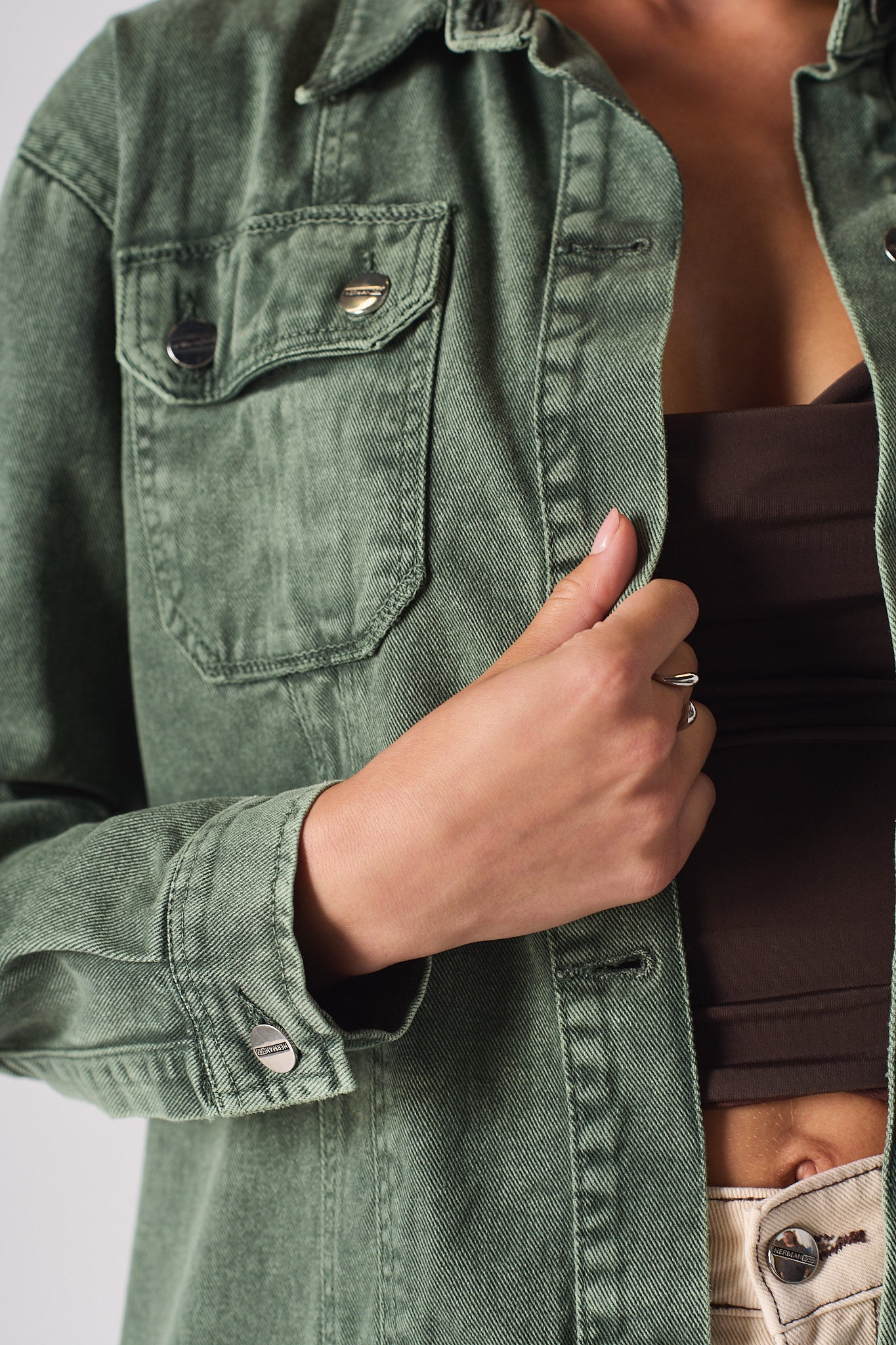 Detailed view of the chest pocket and branded buttons on the green denim shirt.