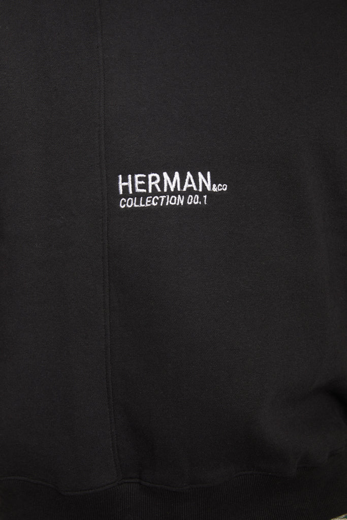 Close-up of the white 'Herman' logo on the front of the men's black jumper.