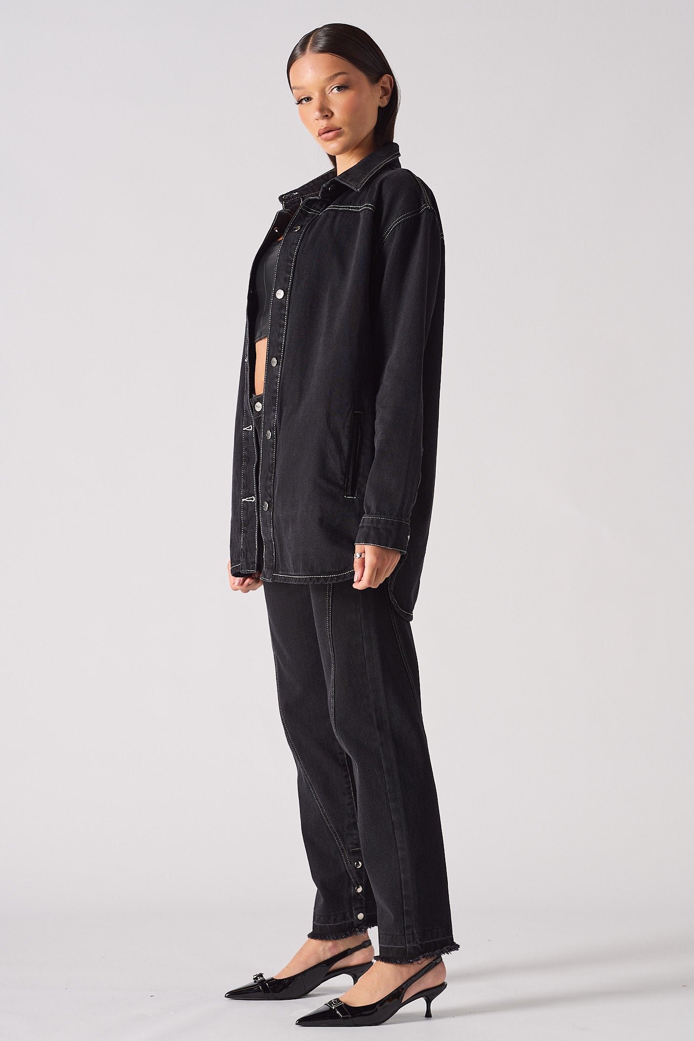 Side profile of the women's oversized black denim shirt showing its length.