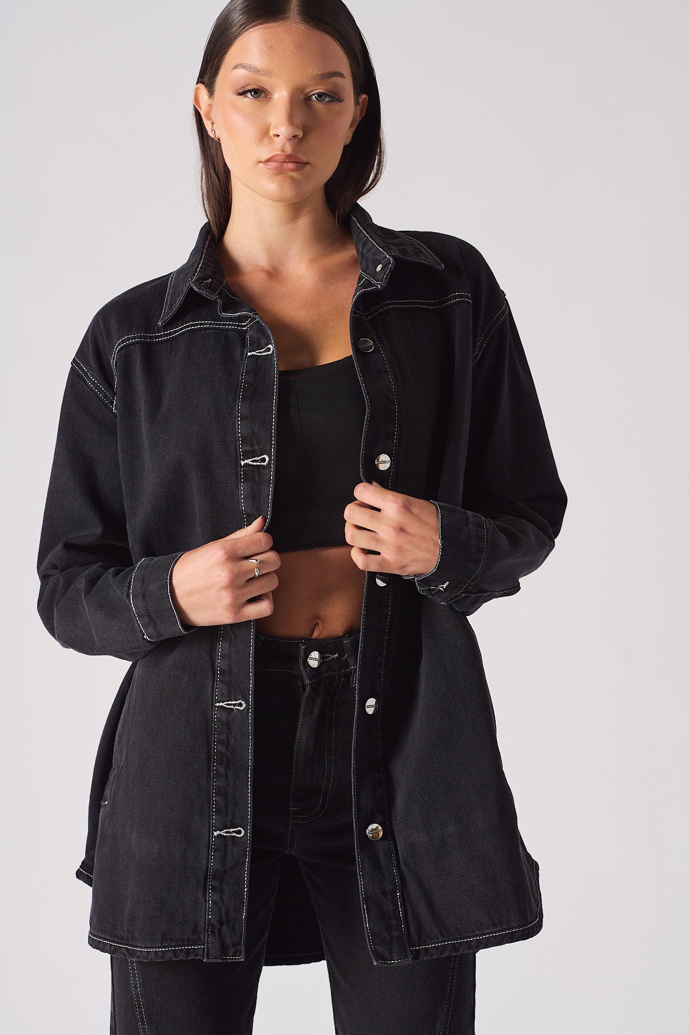 A model styling the black contrast stitch denim shirt worn open.