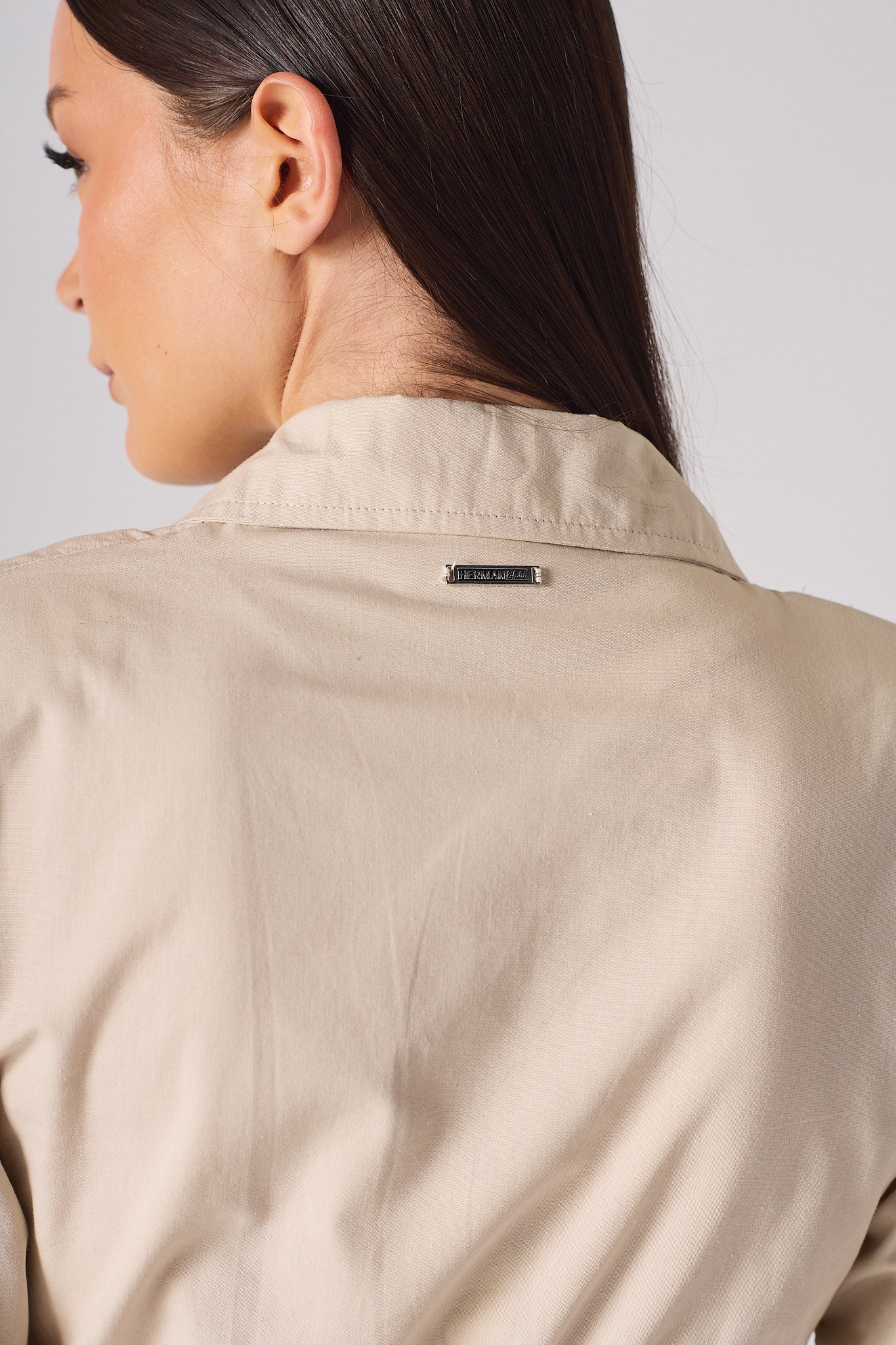 Close-up of the metal logo tag on the back of the women's beige shirt dress.