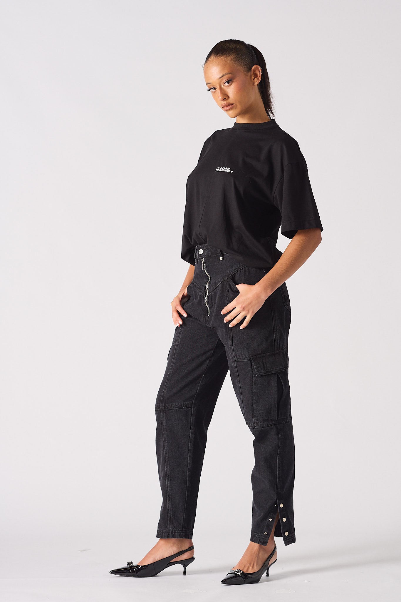 Side profile of a model wearing the women's black cargo jeans with a popper hem.