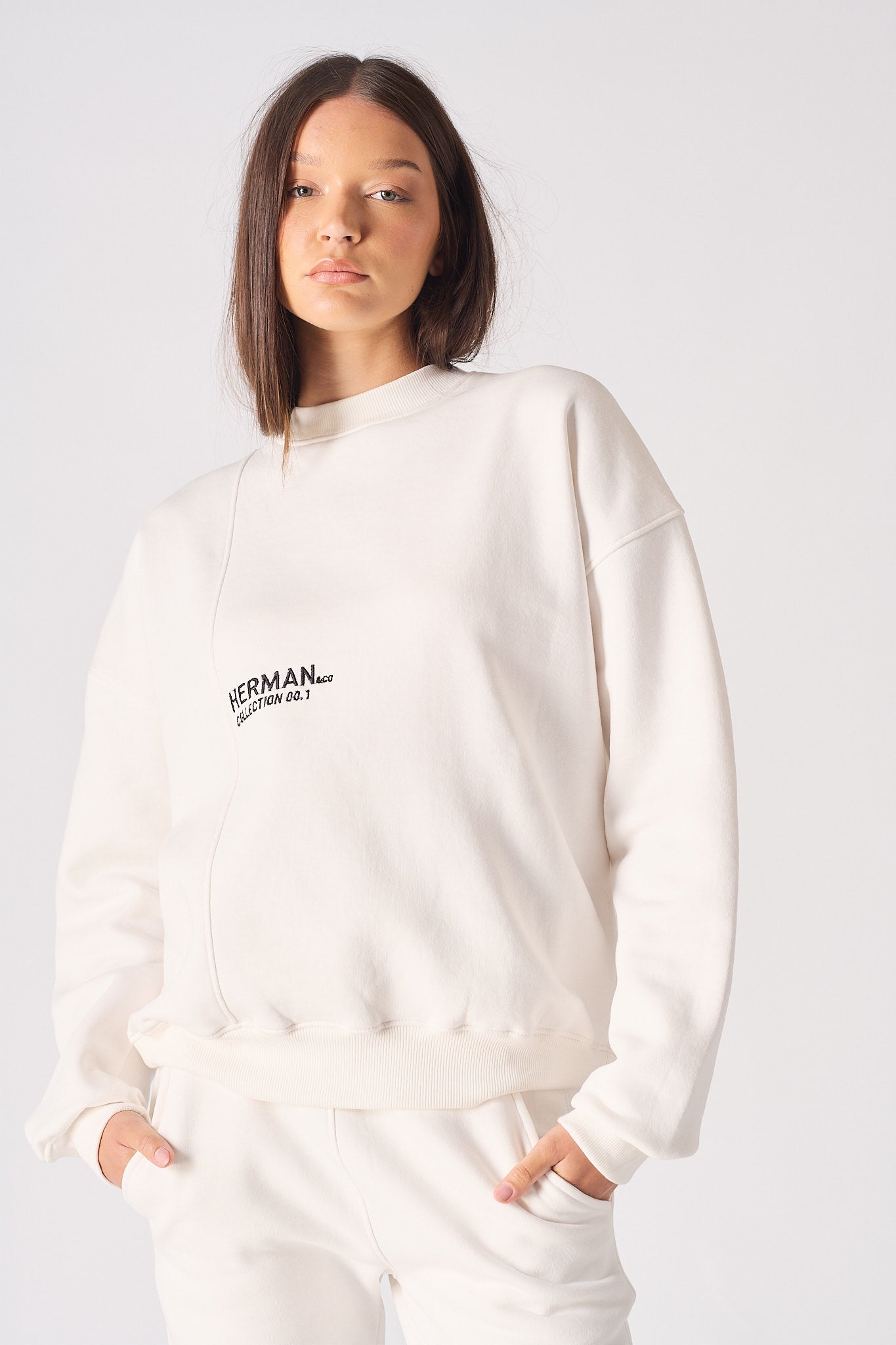 Full length view of model styling the white crewneck sweatshirt with dark trousers