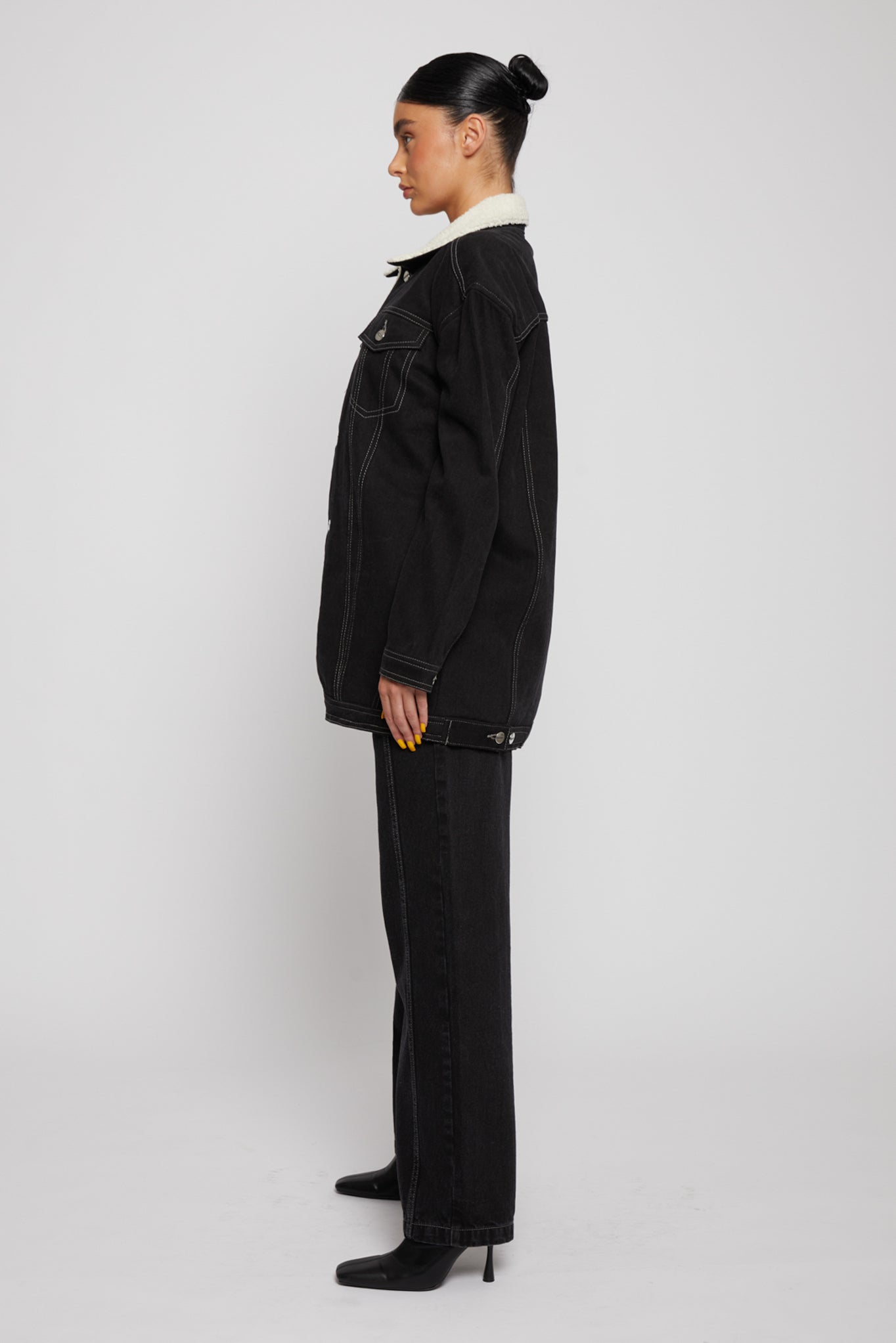 Side profile of the black shearling denim jacket showing its length and fit.