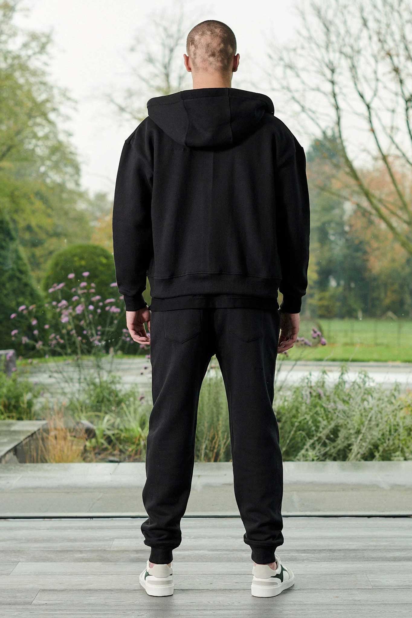 Rear full body view of model wearing a relaxed fit black zip up hoodie men
