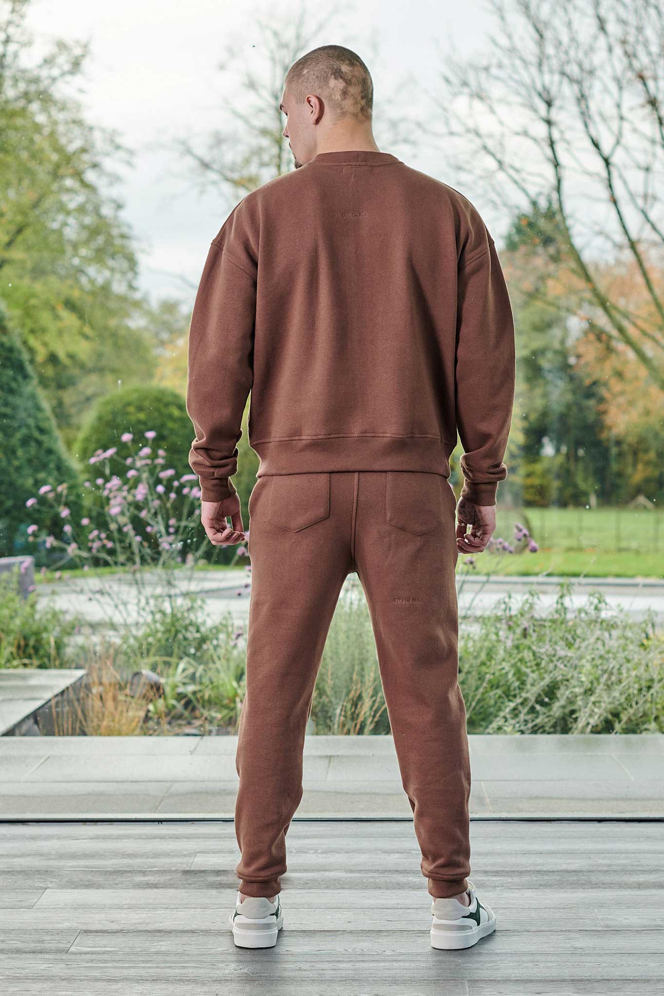 Back view of a model in the men's brown crew neck jumper and tracksuit.