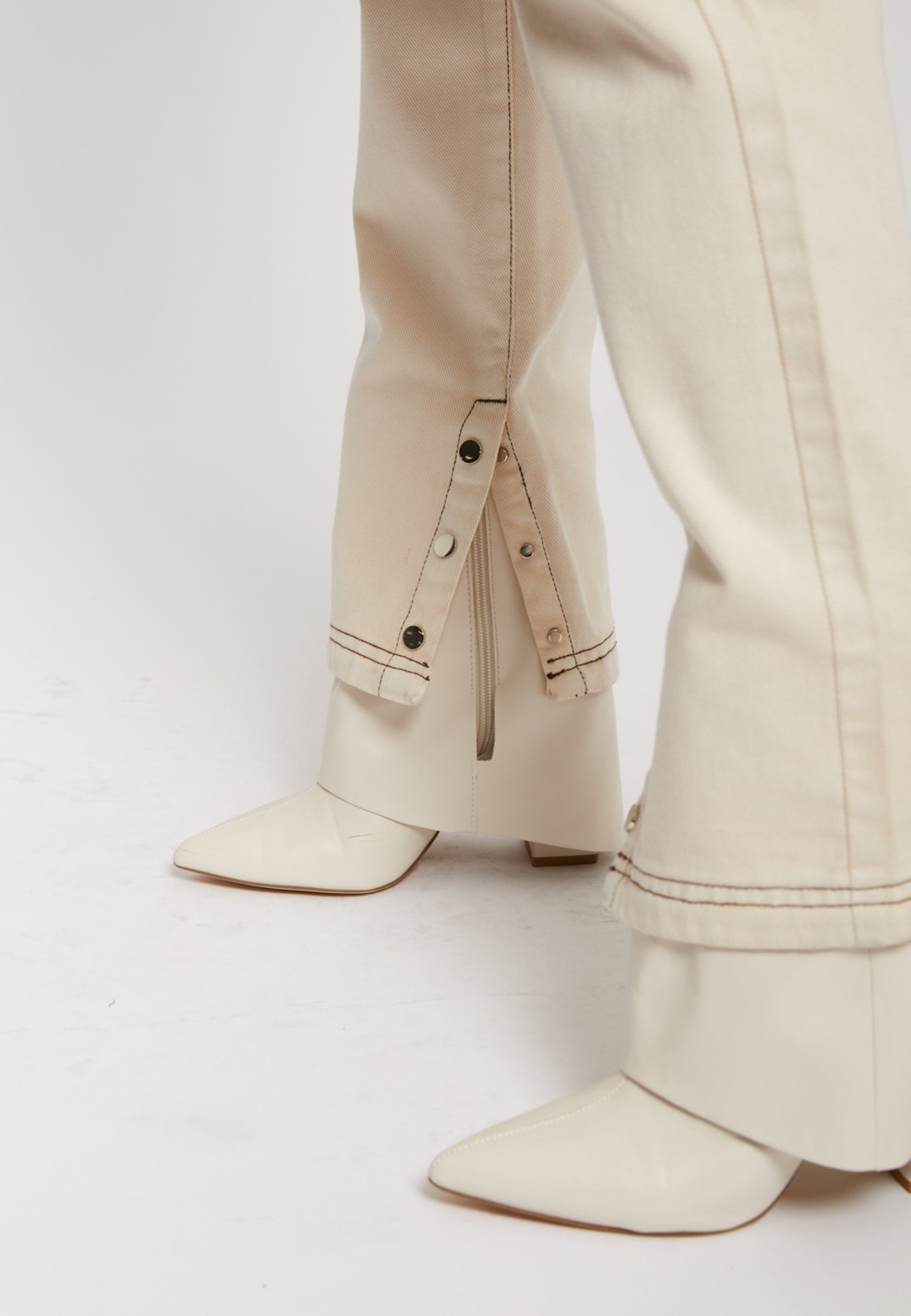 Detailed view of the popper and zip detail on the hem of the ecru jeans