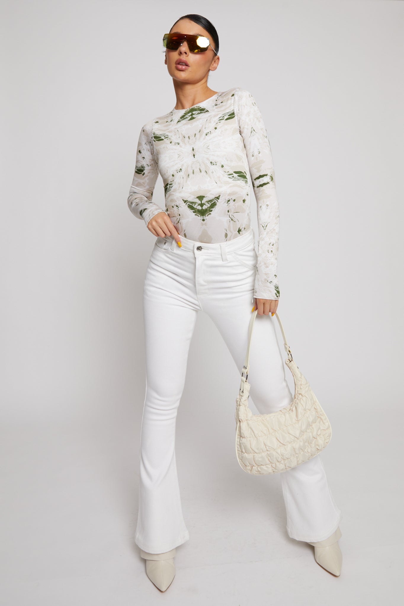 A model styled in high-waisted white flare jeans with a printed top and handbag.