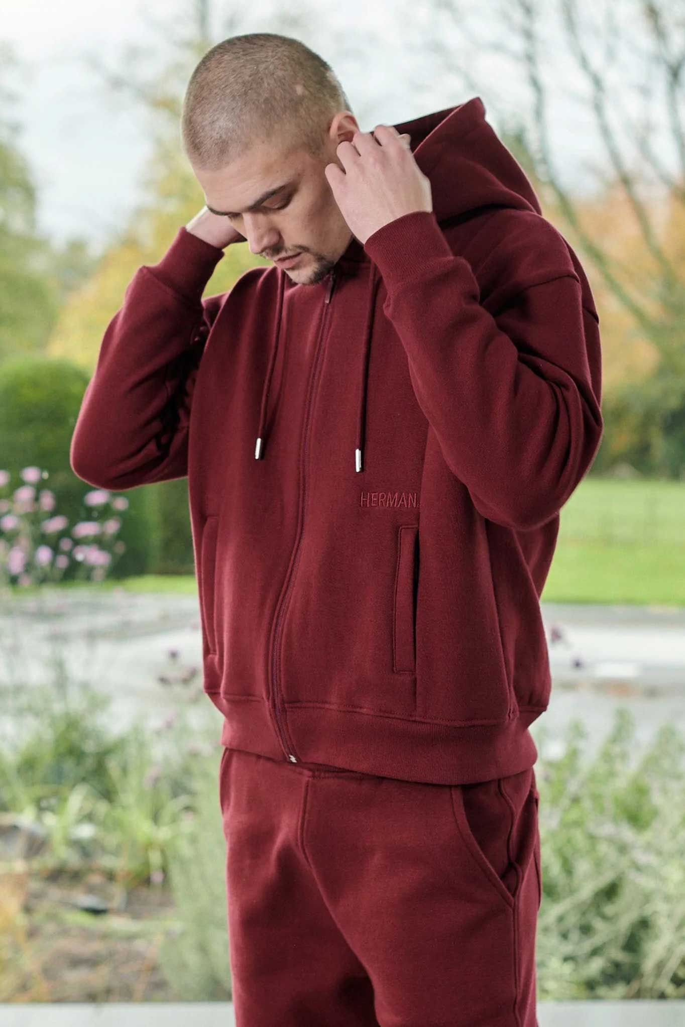 A model adjusting the hood of the men's maroon zip-up hoodie.