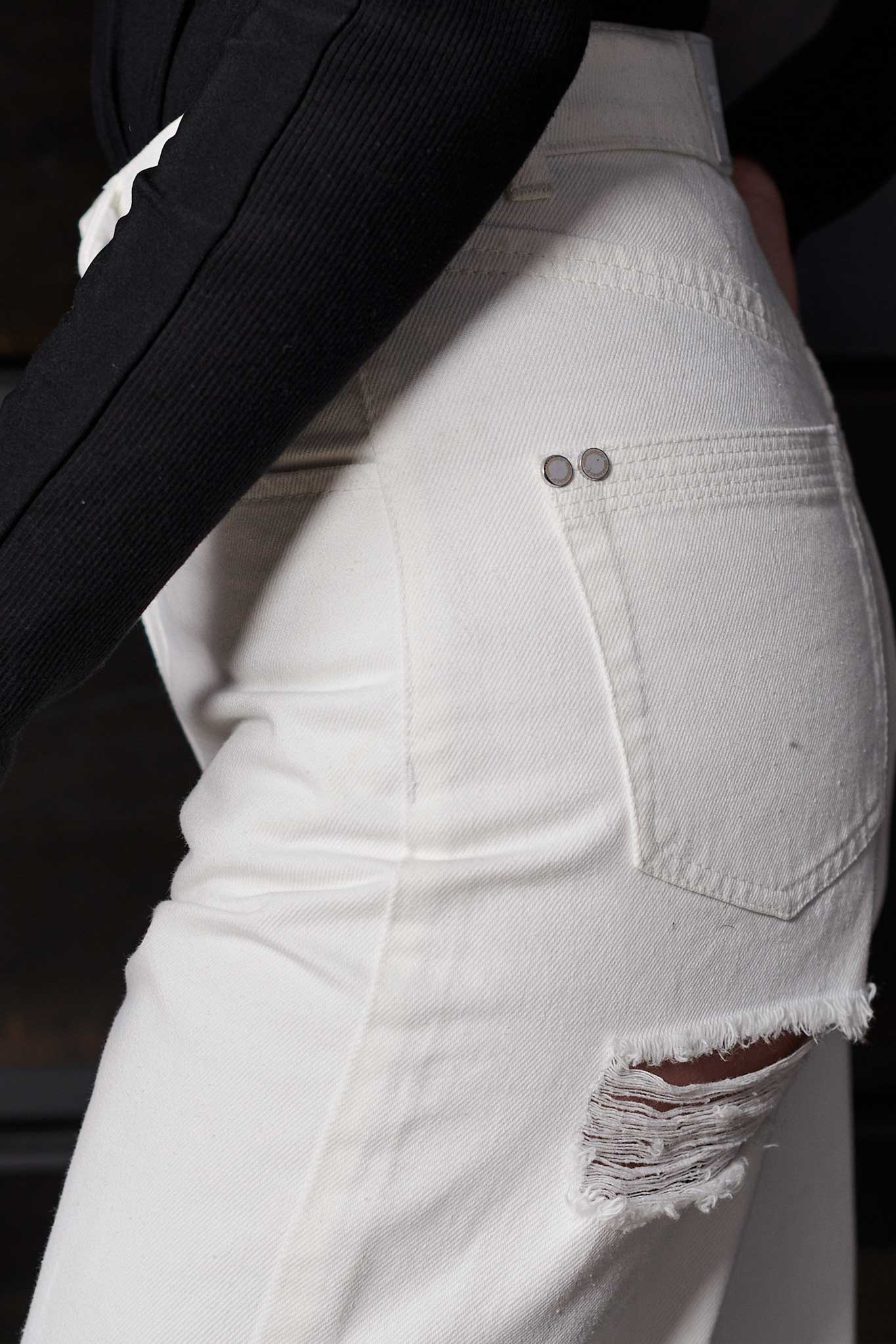 Side view showing the hip and distressed details on the off-white jeans.