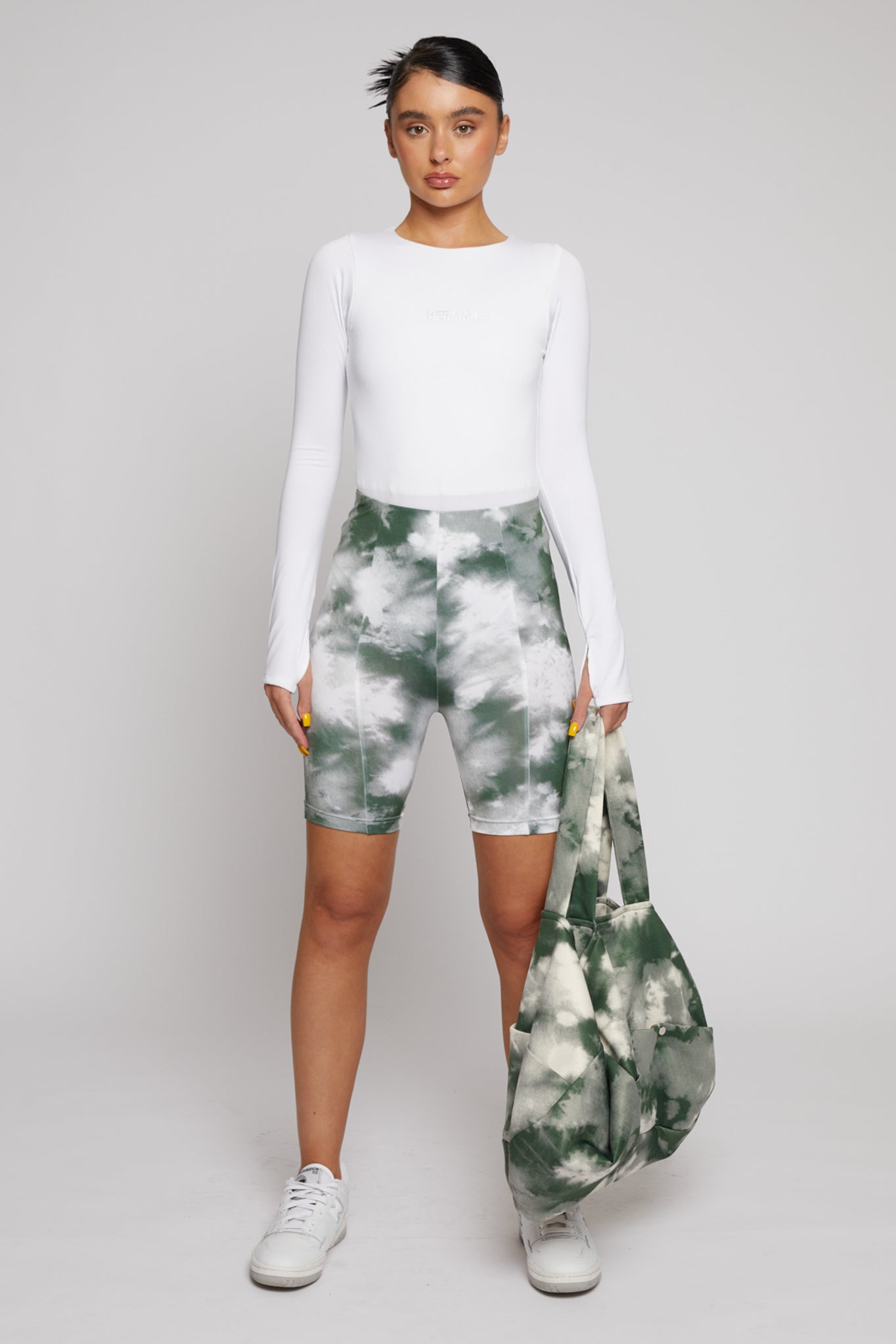 A model styled with the green tie-dye cycling shorts and a matching bag.