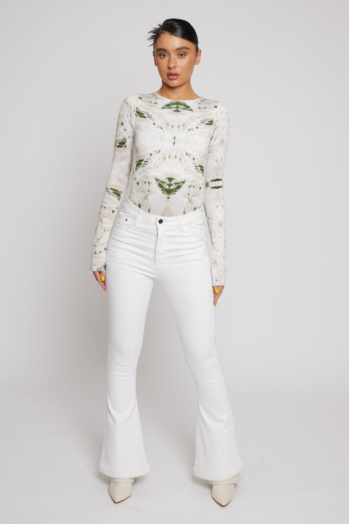 A model styling the high-waisted white flared jeans with a printed top.