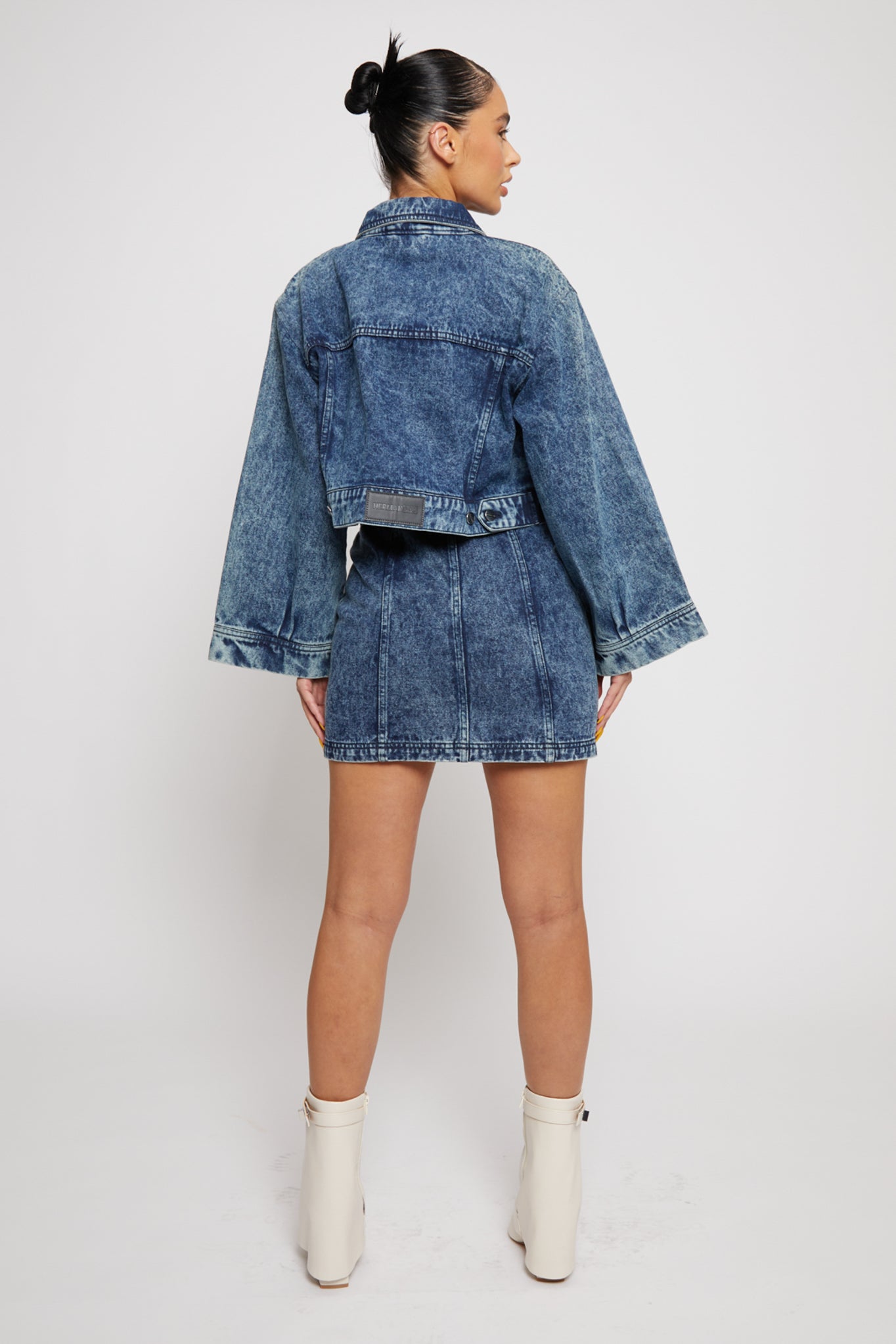 Back view of a model in the wide arm acid wash denim jacket and skirt.