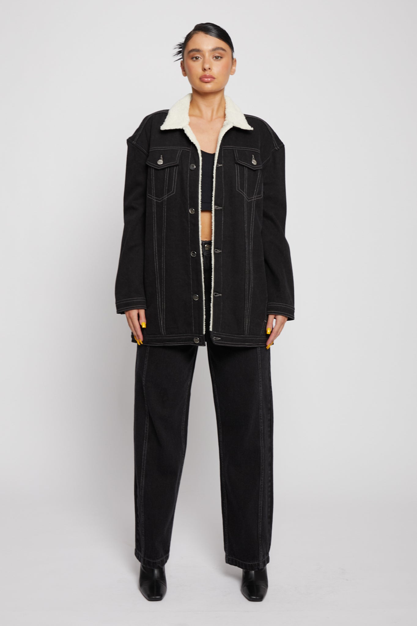 Front view of a model wearing the women's black denim jacket with a shearling collar.