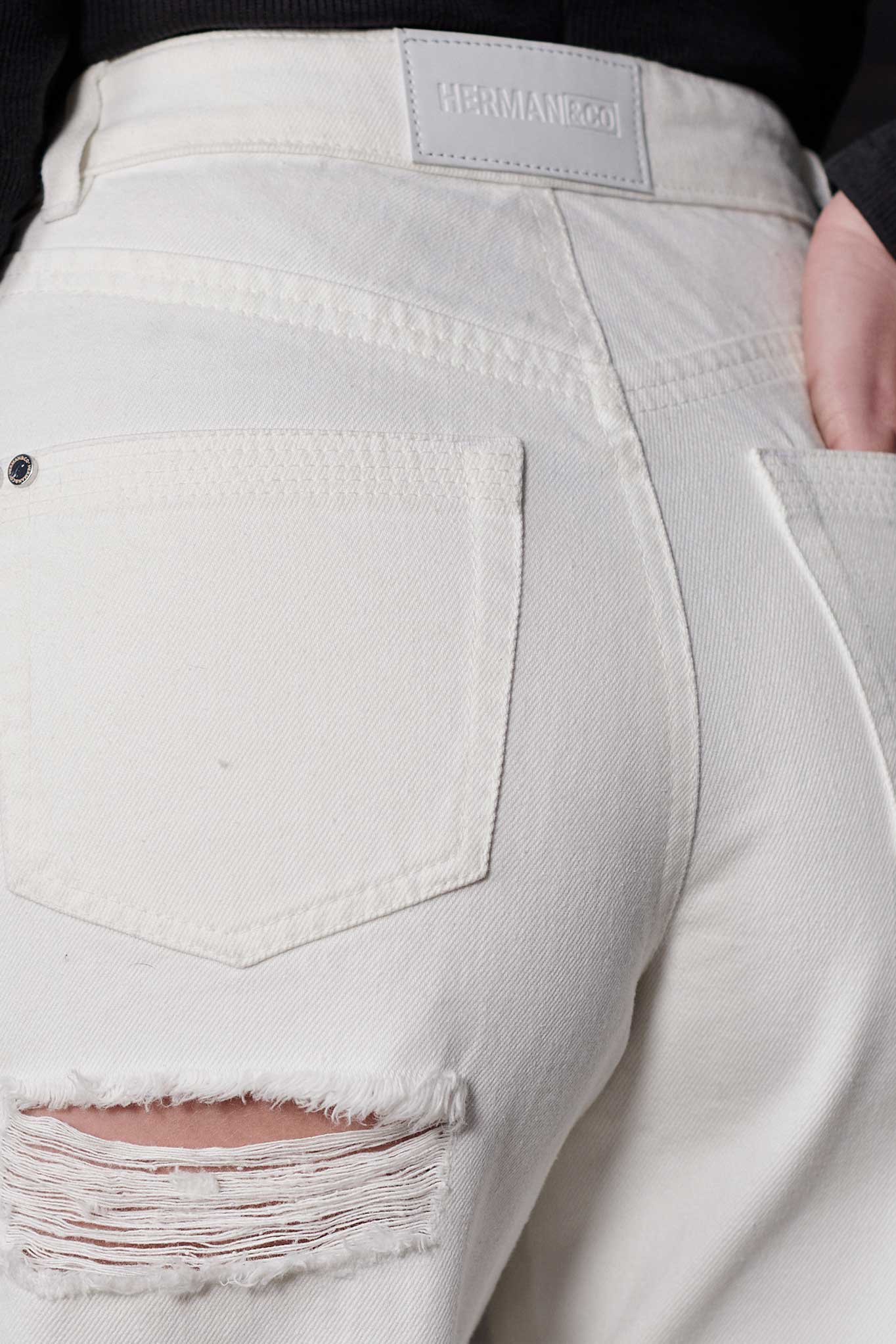 Detailed view of the rip and distressing under the back pocket of the jeans.