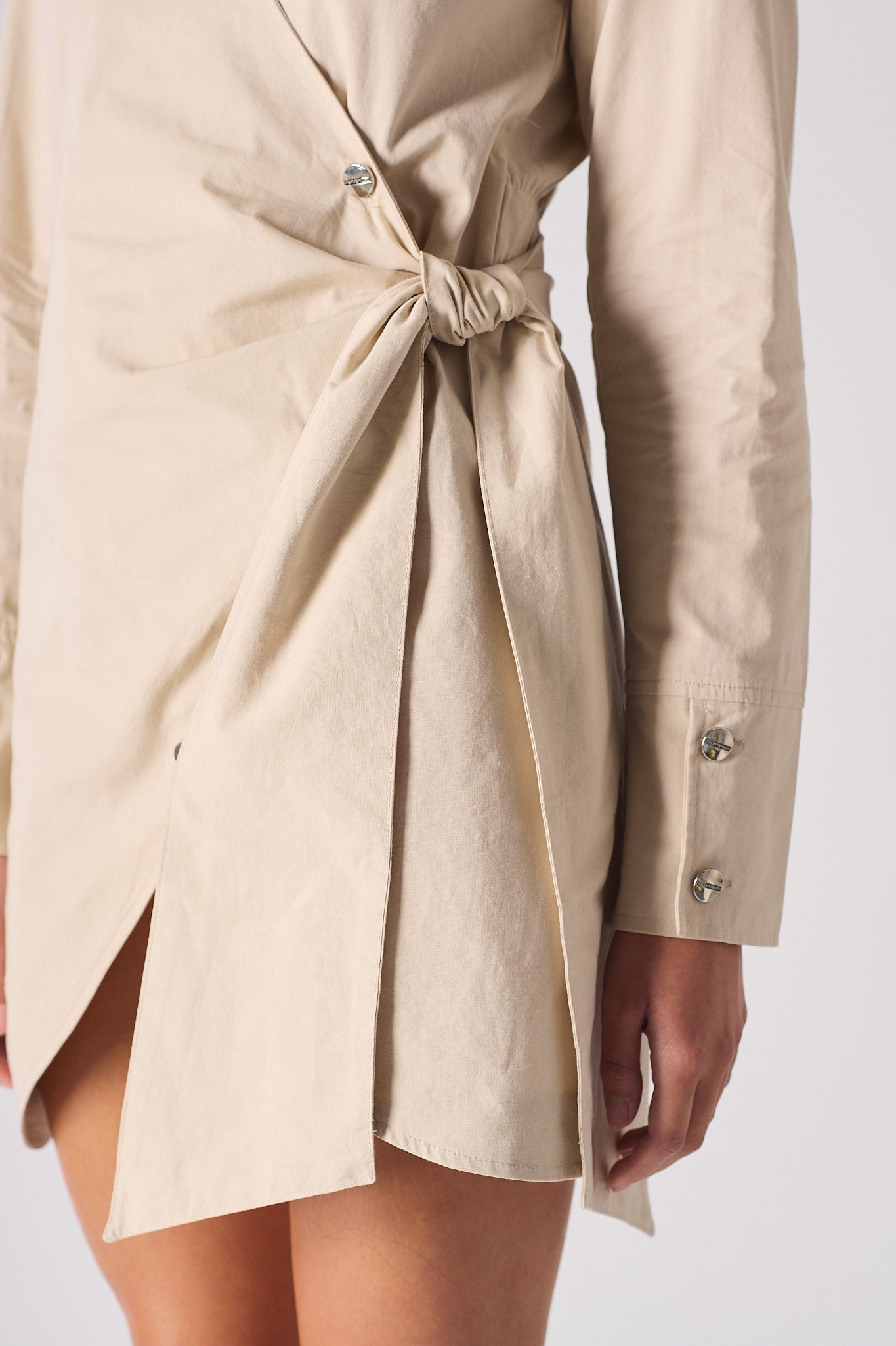 Close-up of the tie waist and side slit on the beige asymmetric dress.