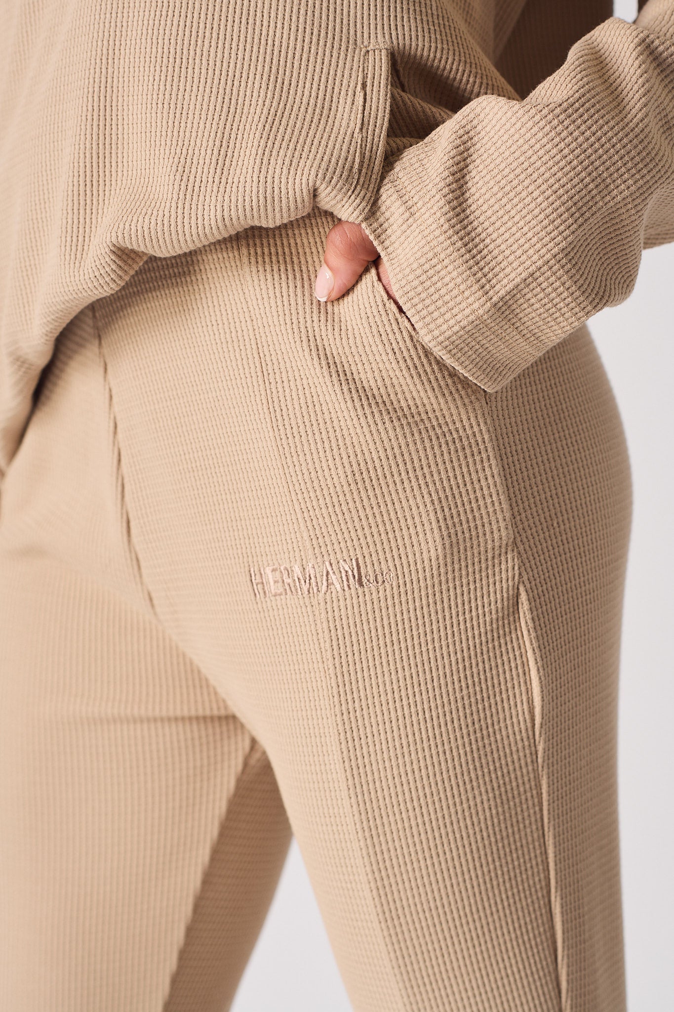 Close-up shot of the embroidered Herman & Co logo on the beige waffle joggers