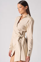 Side profile of a model in the women's beige wrap-style asymmetric shirt dress.