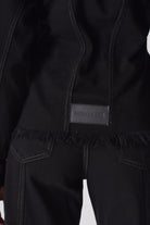 Close-up of the logo patch on the back of the black denim jacket.