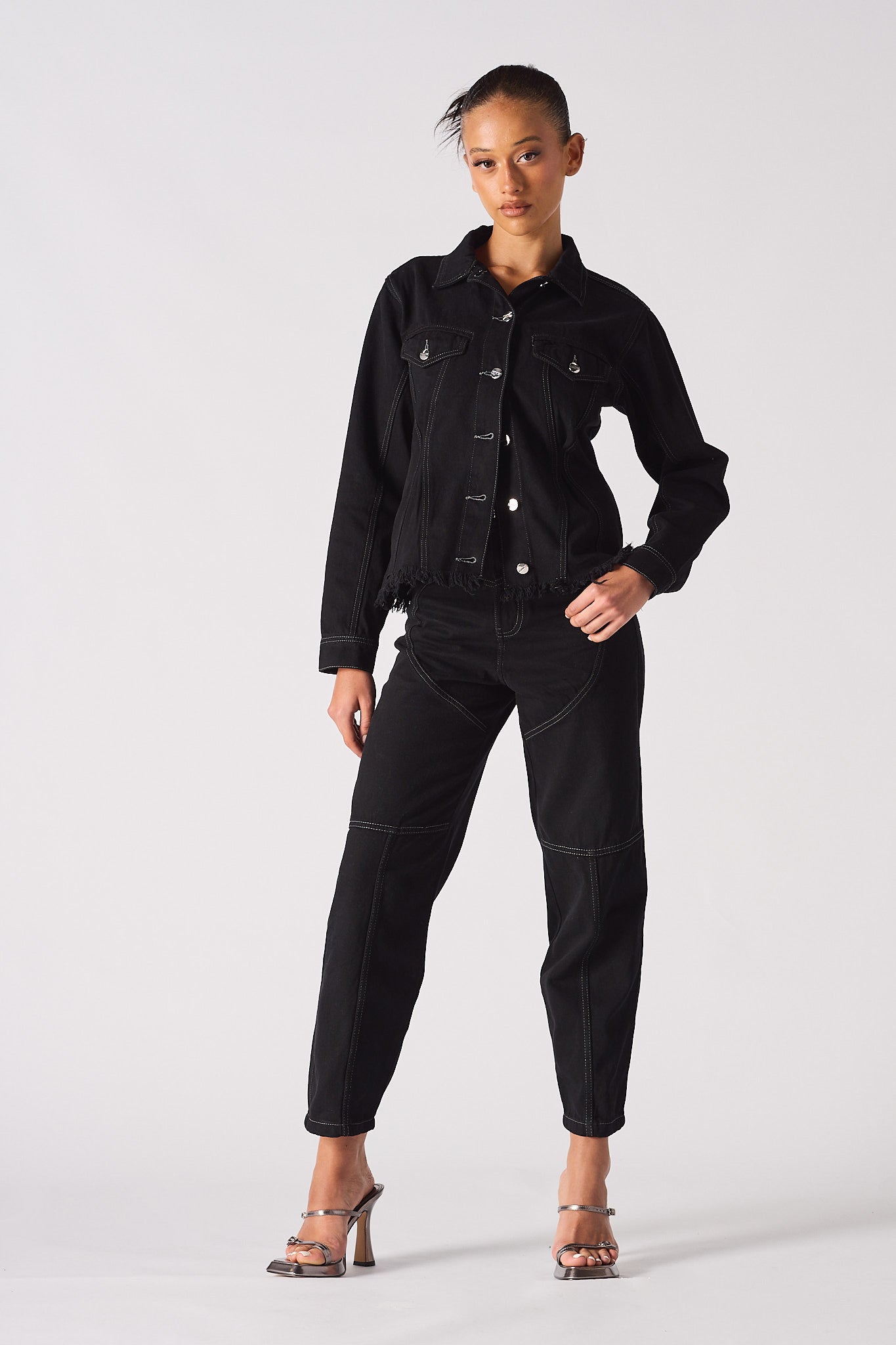 Full view of a model styled in the black denim jacket with a tapered waist.