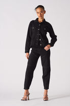 Full view of a model styled in the black denim jacket with a tapered waist.