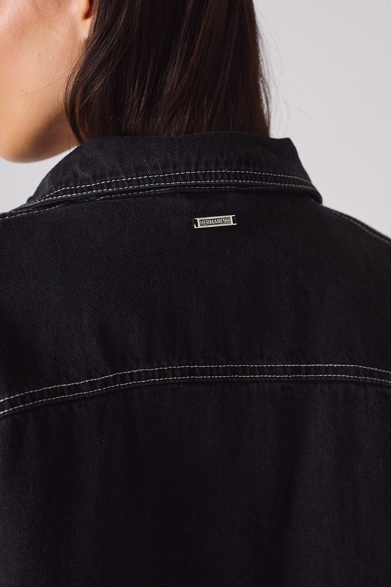 Close-up of the metal logo tag on the back of the black denim shirt.