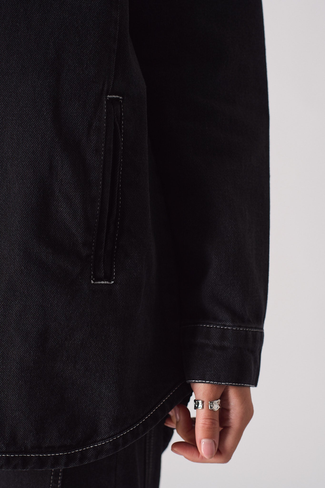 Close-up of the side pocket and curved hem on the black denim shirt.