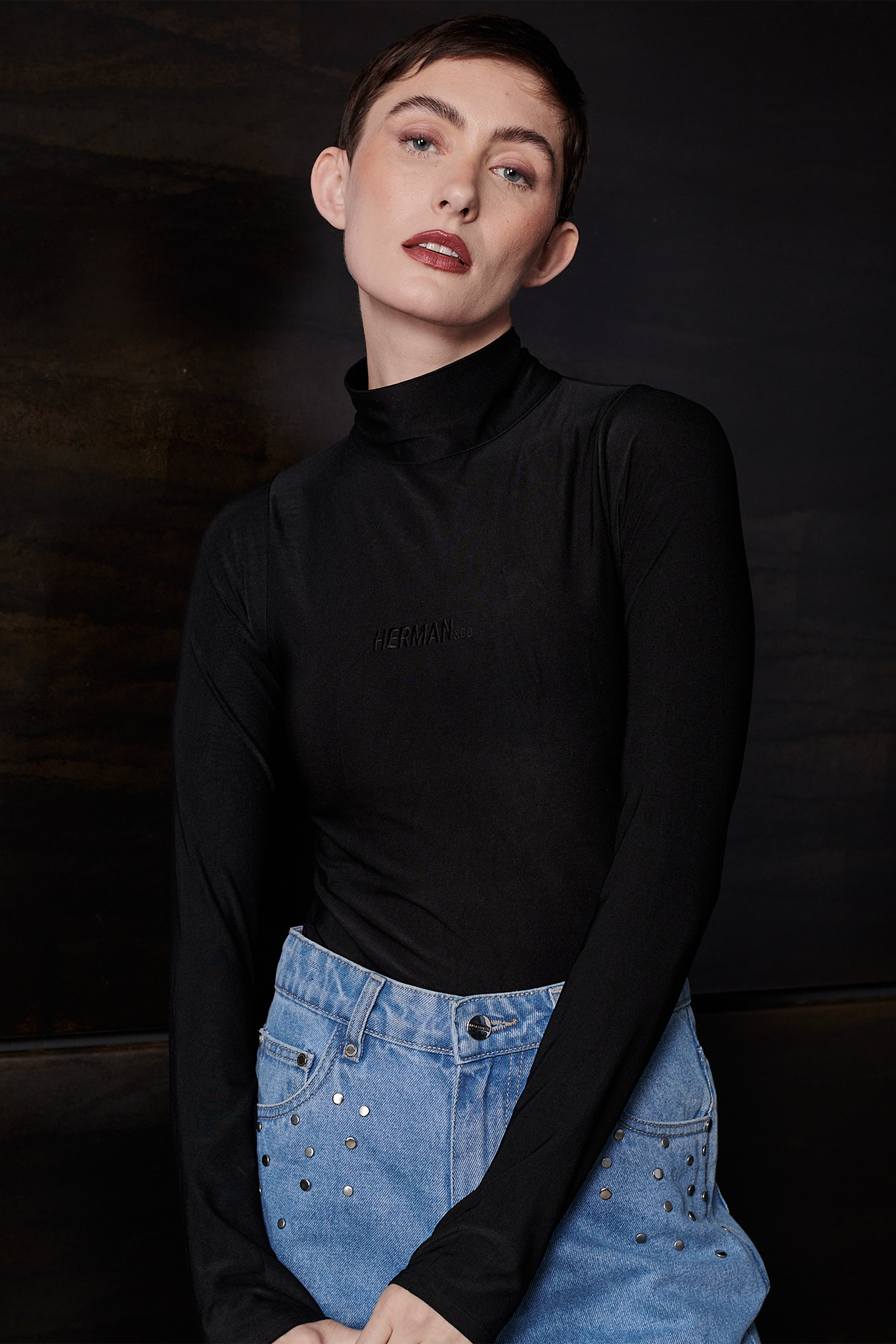 A model wearing the black spandex bodysuit with a turtleneck and jeans.