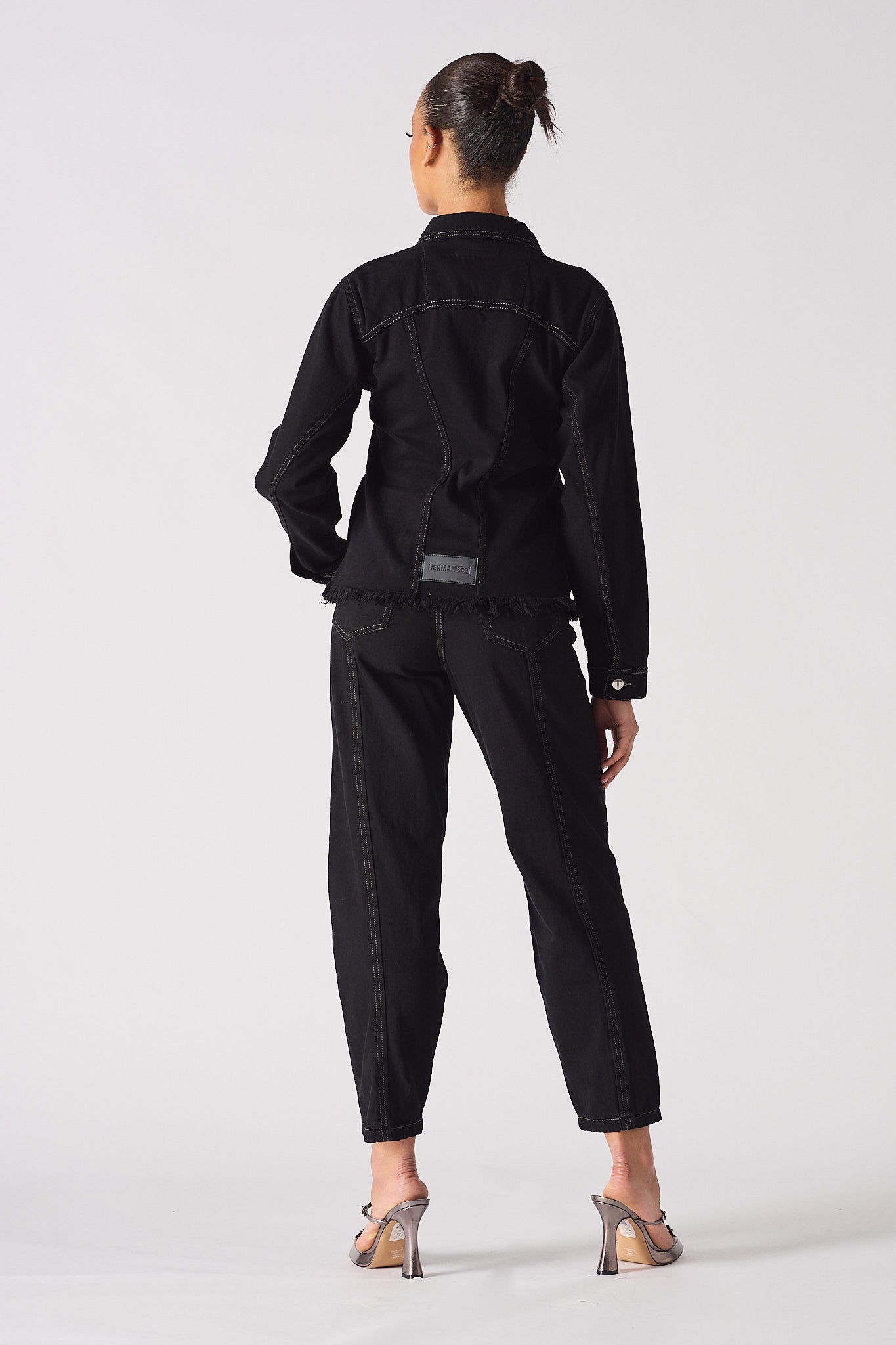 Back view of a model wearing the black tapered waist denim jacket.