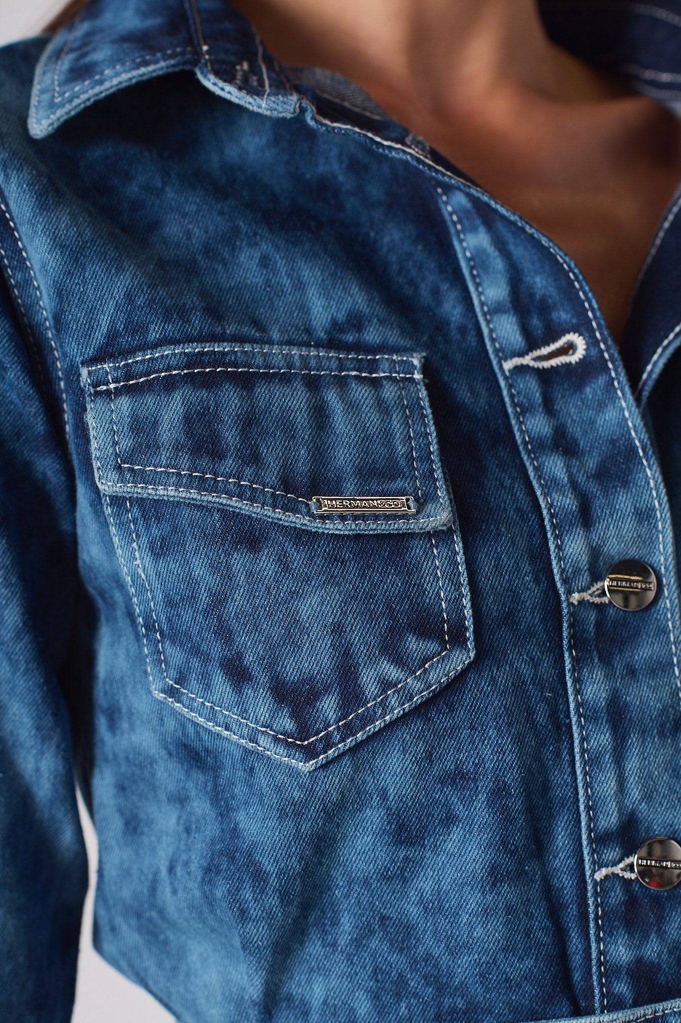 Super close-up of the Herman & Co metal tag on the pocket of the blue denim dress
