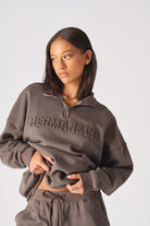 Close up of the embossed chest logo on brown half zip women's sweatshirt