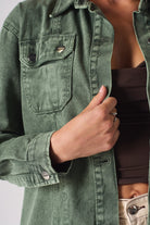 Detailed view of the chest pocket and branded buttons on the green denim shirt.