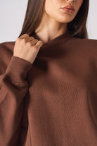 Detail of the tonal logo embroidery on the chest of brown crew neck jumper