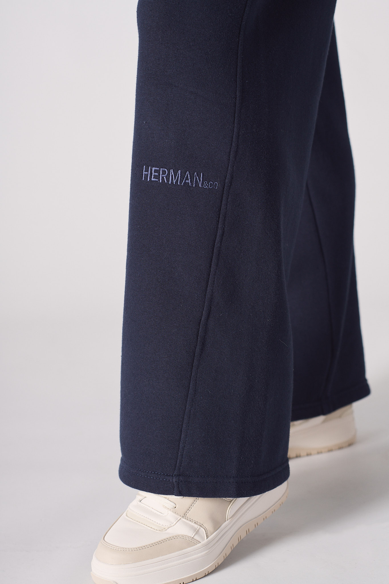 Close-up of the tonal embroidered logo on the navy wide-leg joggers.