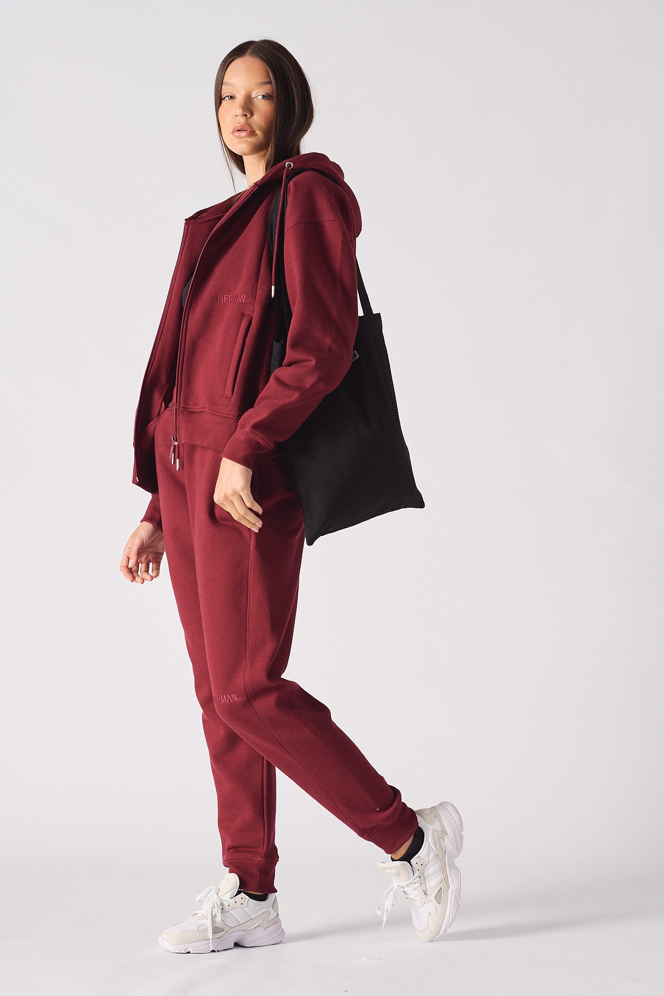 A model styled in the ladies' red zip-up hoodie with a tote bag.