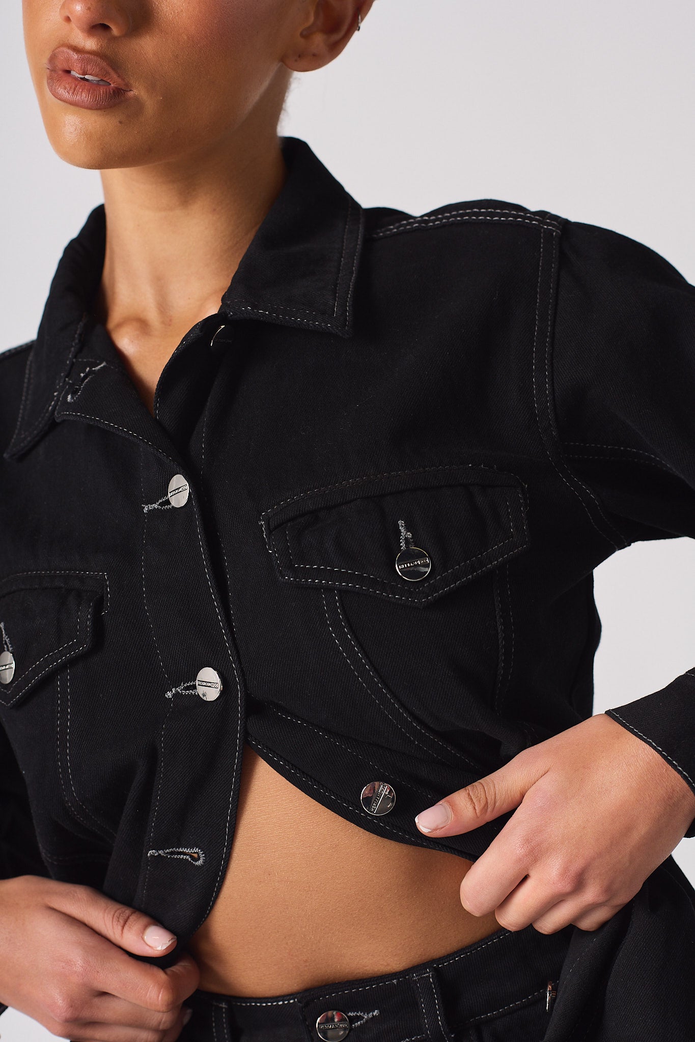 Close-up of the button and pocket detail on the tapered waist denim jacket.