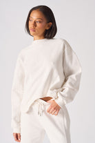 Mid shot of women wearing a white crew neck jumper with curved hem detail