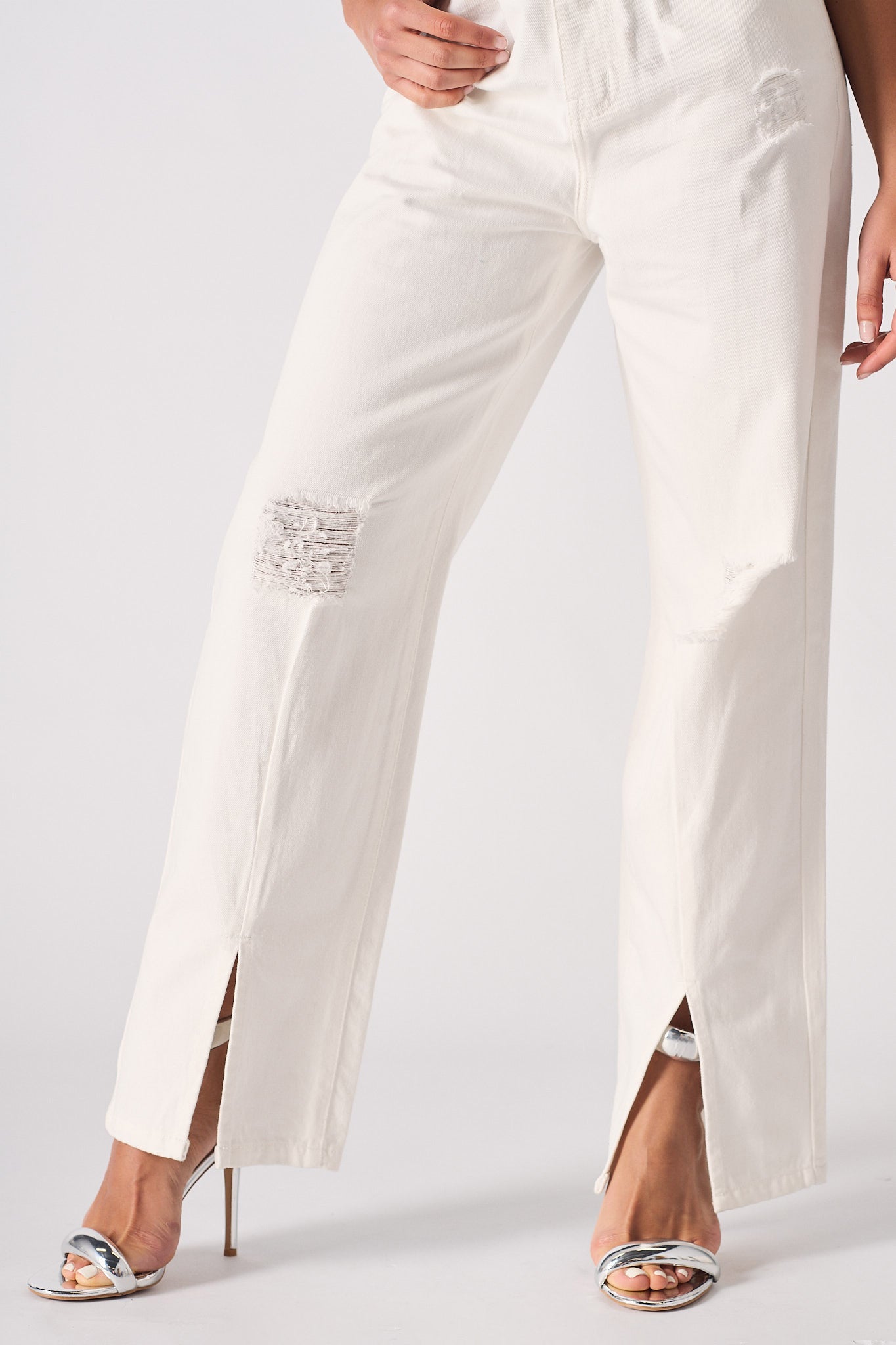 Close-up of the distressed details and the split hem on the white jeans.