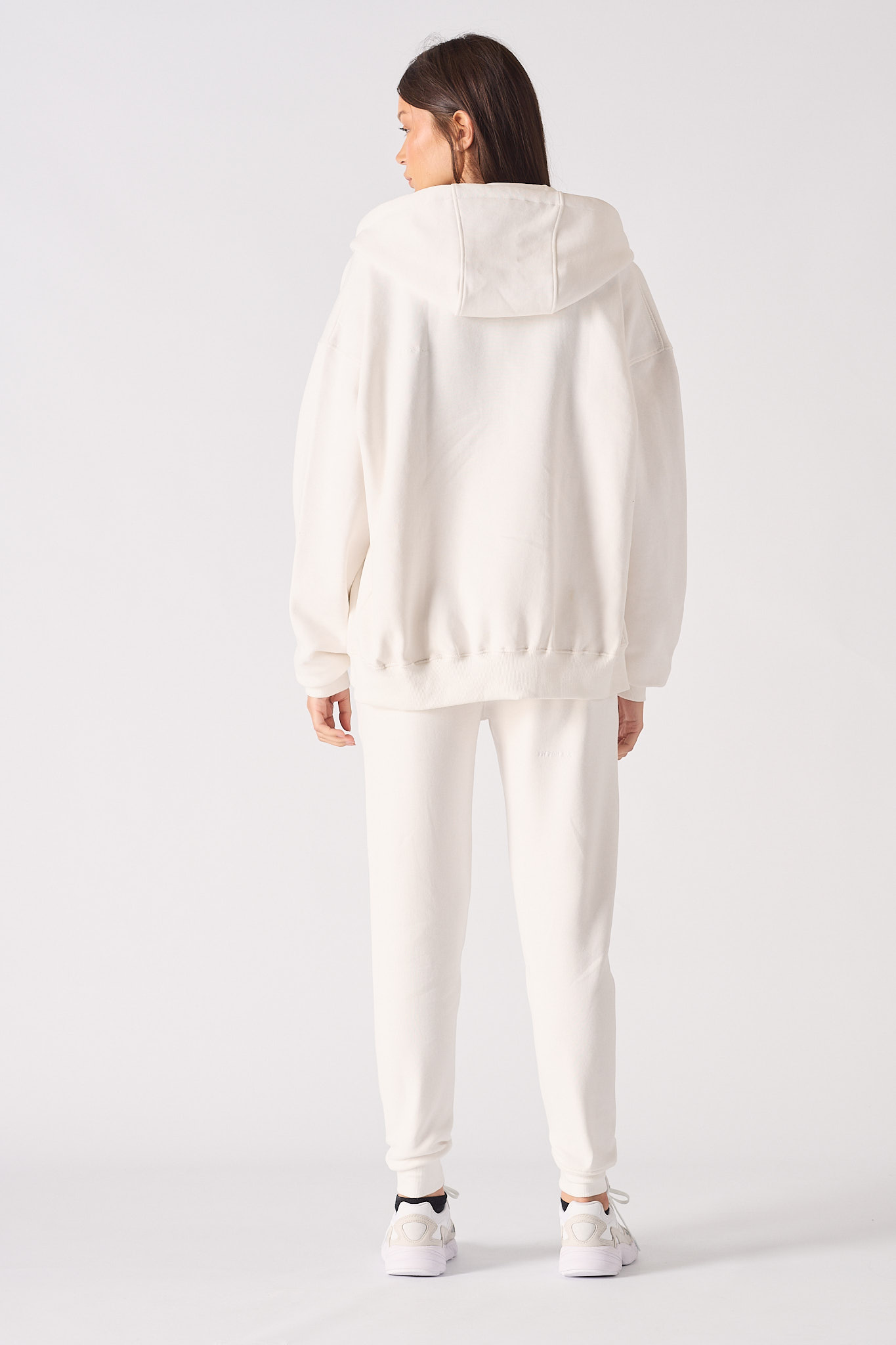 Back view of a model in the women's white zip-up hoodie and matching joggers.