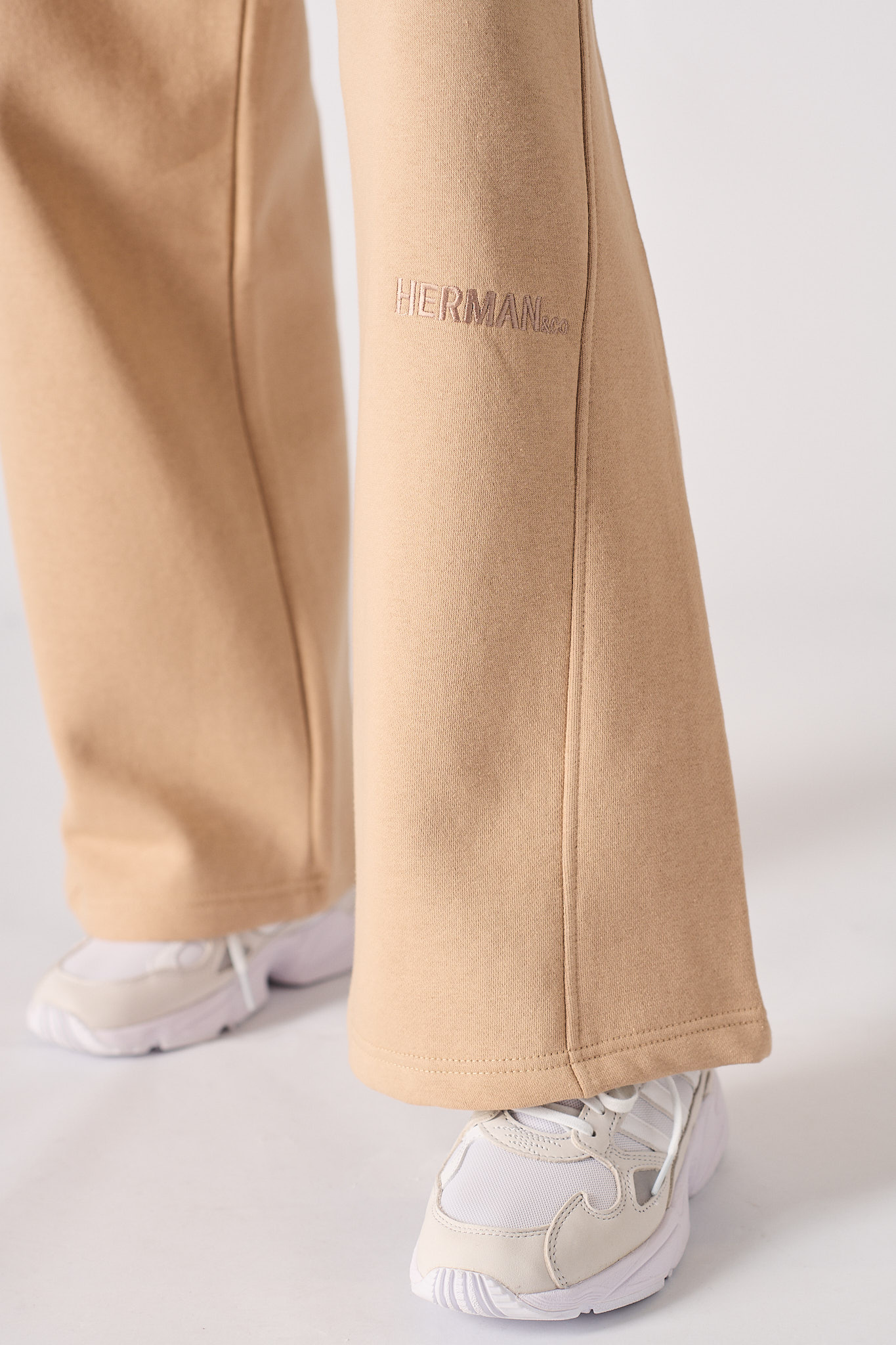 Close-up of the tonal embroidered logo on the wide-leg joggers in beige.