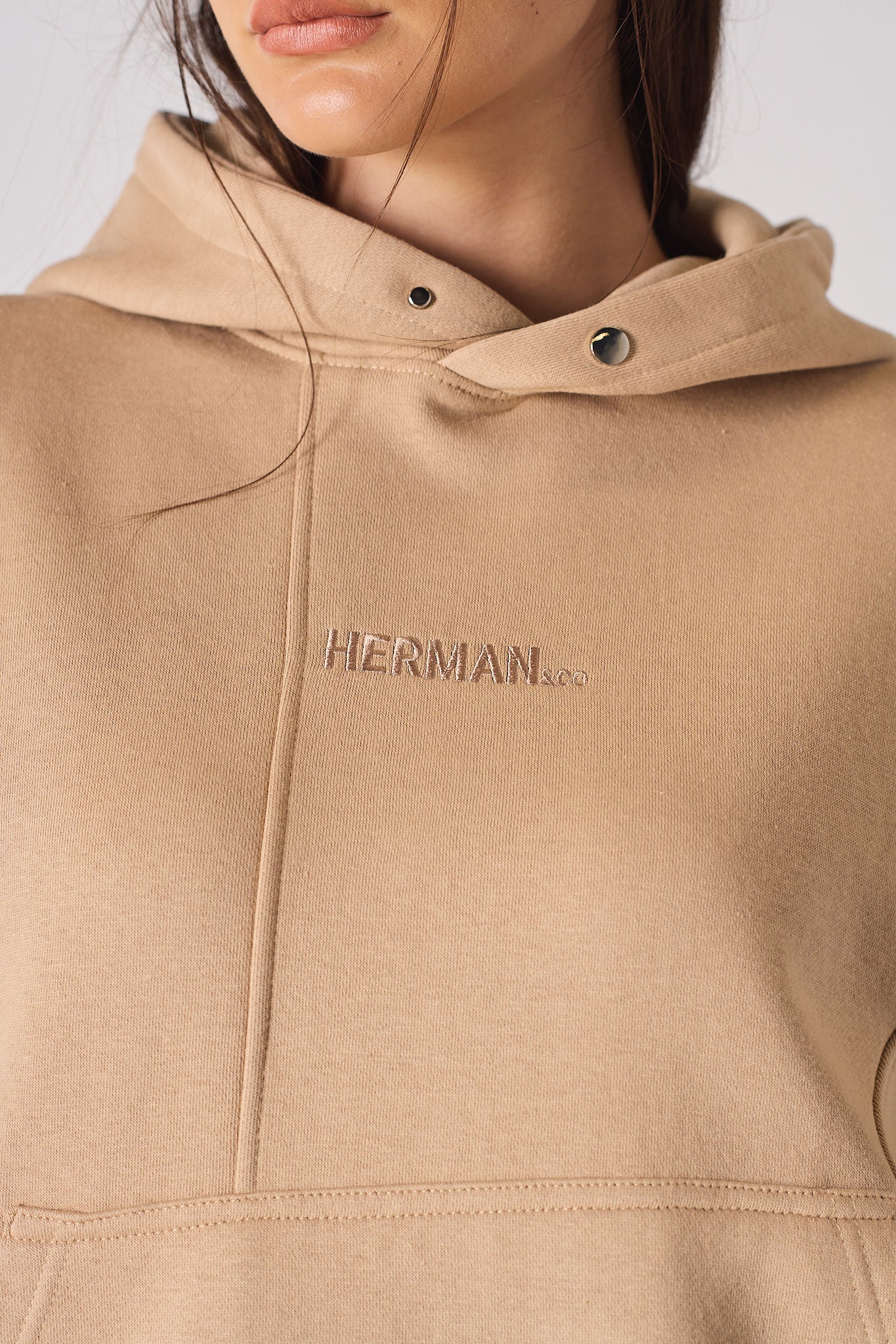 Side view of model with hand in the kangaroo pocket of beige hoodie