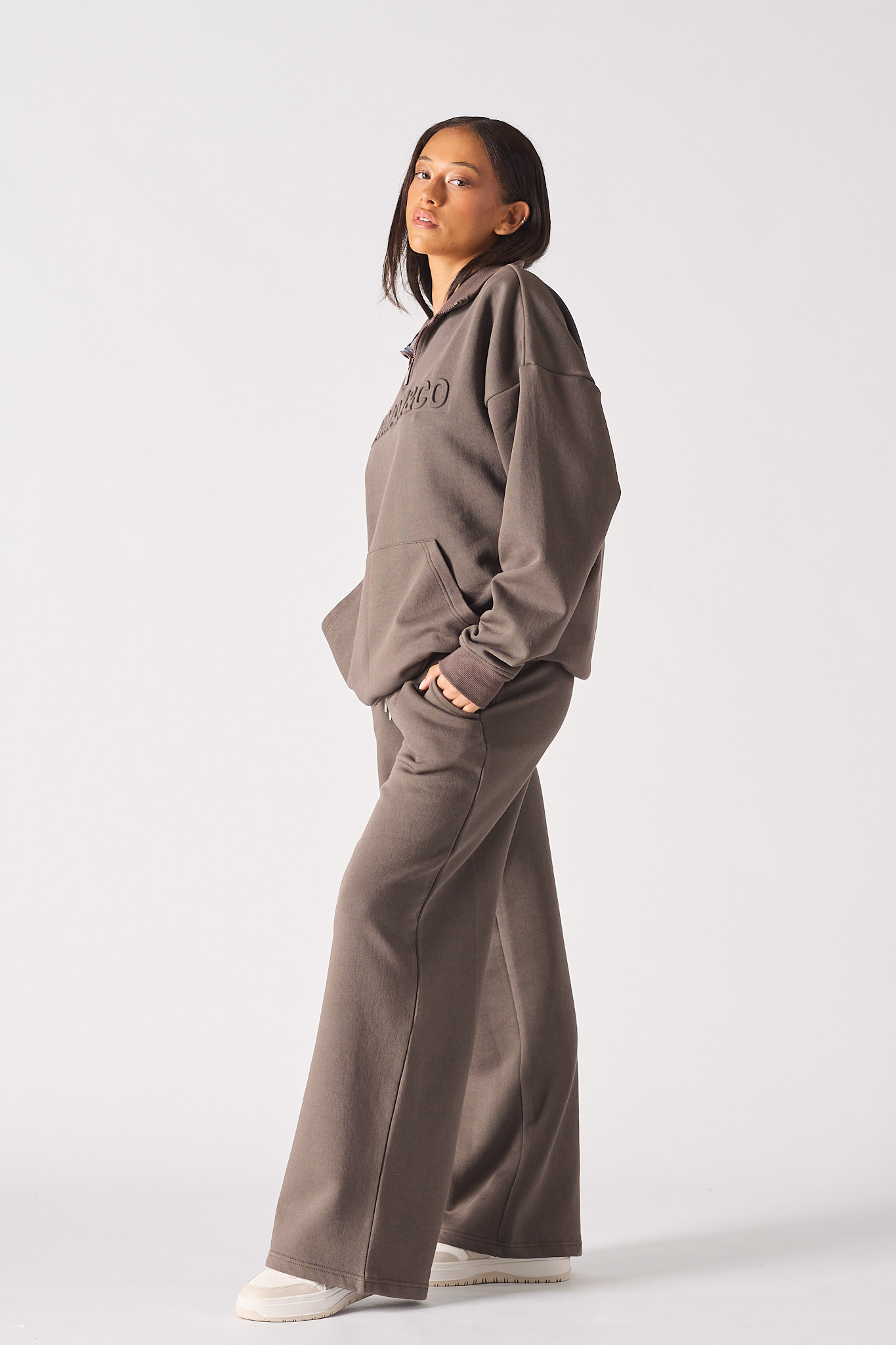 Mid section view of model with hands in pockets of brown half zip sweatshirt