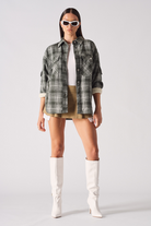 A model styled in the women's dark green checked overshirt with a skirt and boots.