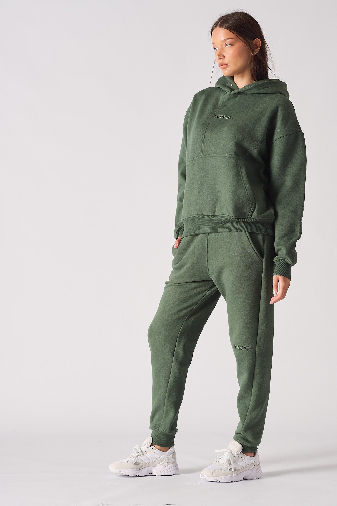 Woman wearing a dark green hoodie and matching joggers standing pose