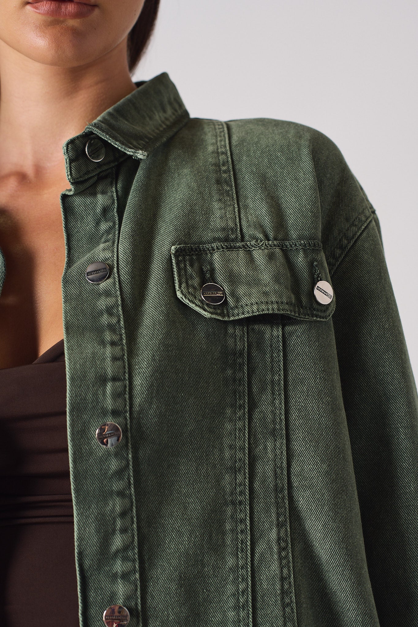 Close-up of the shoulder and button details on the women's green denim shirt.