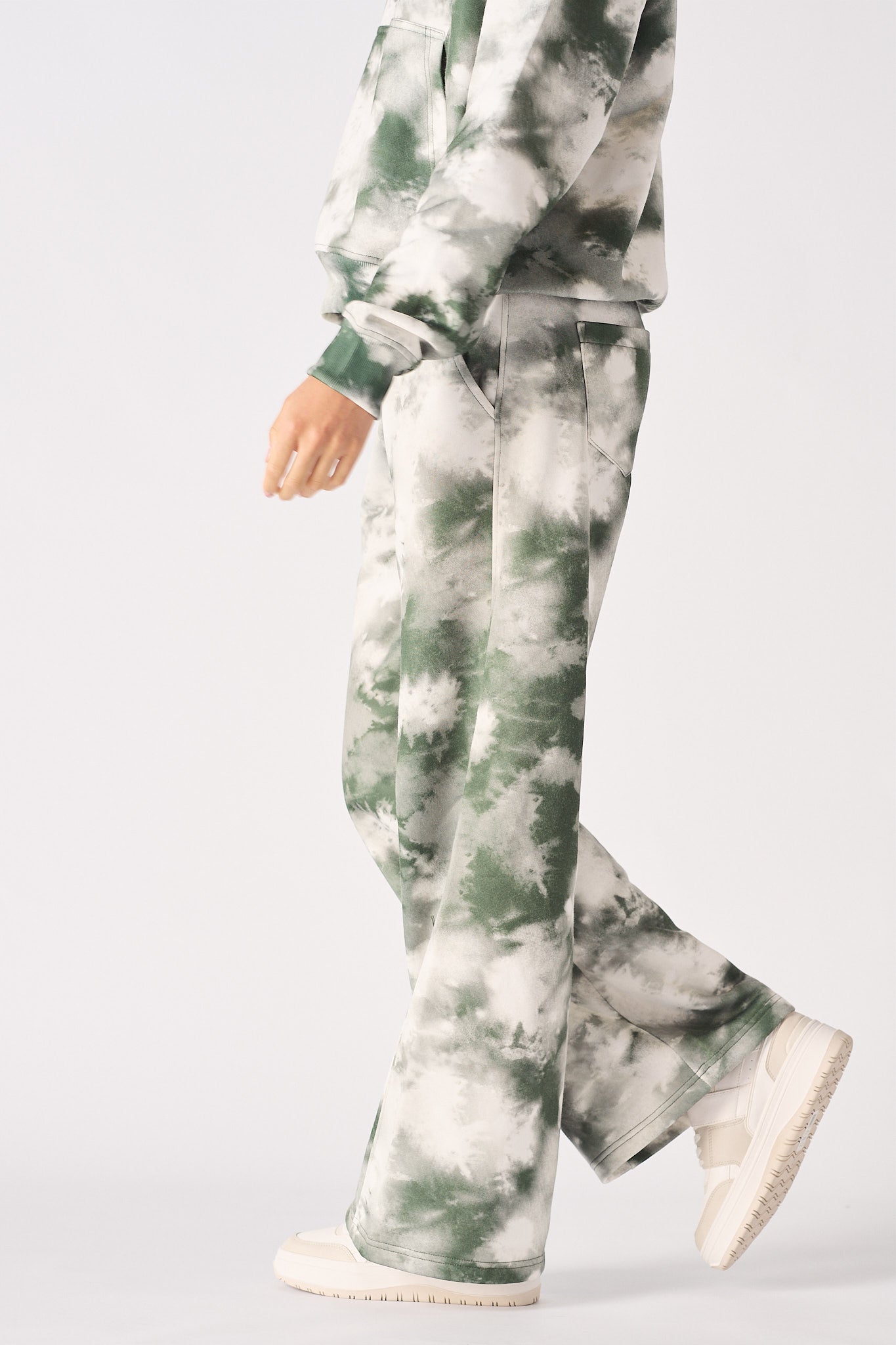 Side profile of a model walking in the women's green tie-dye wide-leg joggers.
