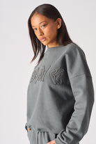 Zoomed in view of the tonal embossed branding on womens oversized grey sweatshirt